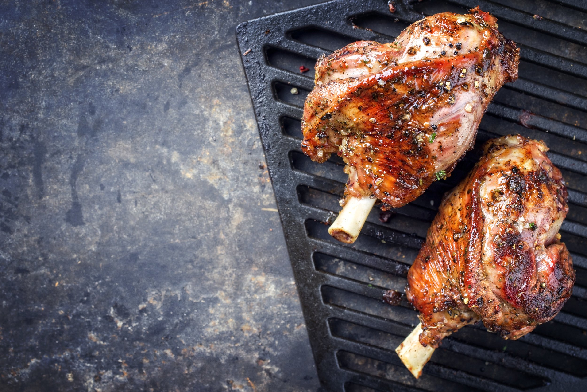 Grilled marinated lamb shanks resting on a cast iron grill, showcasing a golden-brown crust and seasoned with herbs and spices.